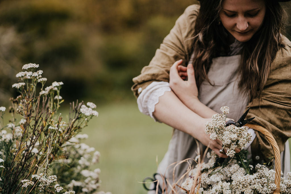 Woman in linen dress collecting yarrow in a basket