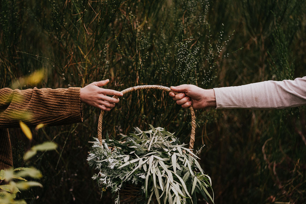 two hands holding a wicker basket full of herbs